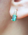 A close up of a yellow gold emerald earring, top accent diamonds in 14k yellow gold on an earlobe