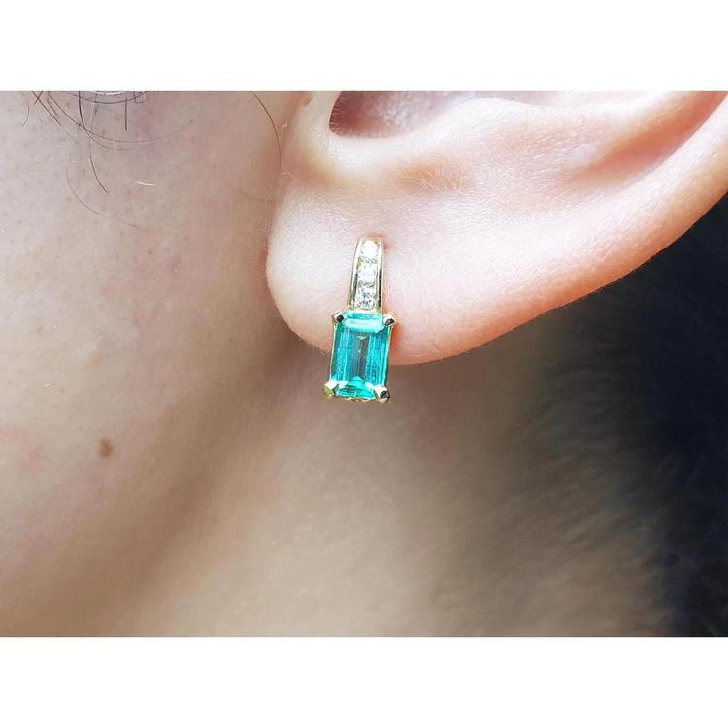 Emerald cut emerald earring in 14K yellow gold with small diamonds, worn on an ear.