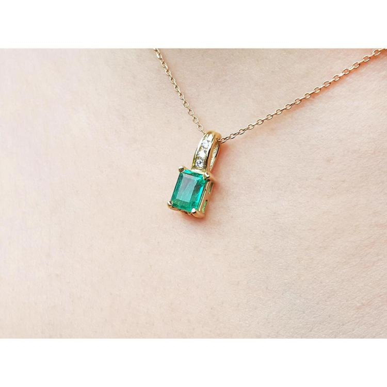 Emerald pendant with diamonds on a 14K yellow gold chain, worn on a person's neck.