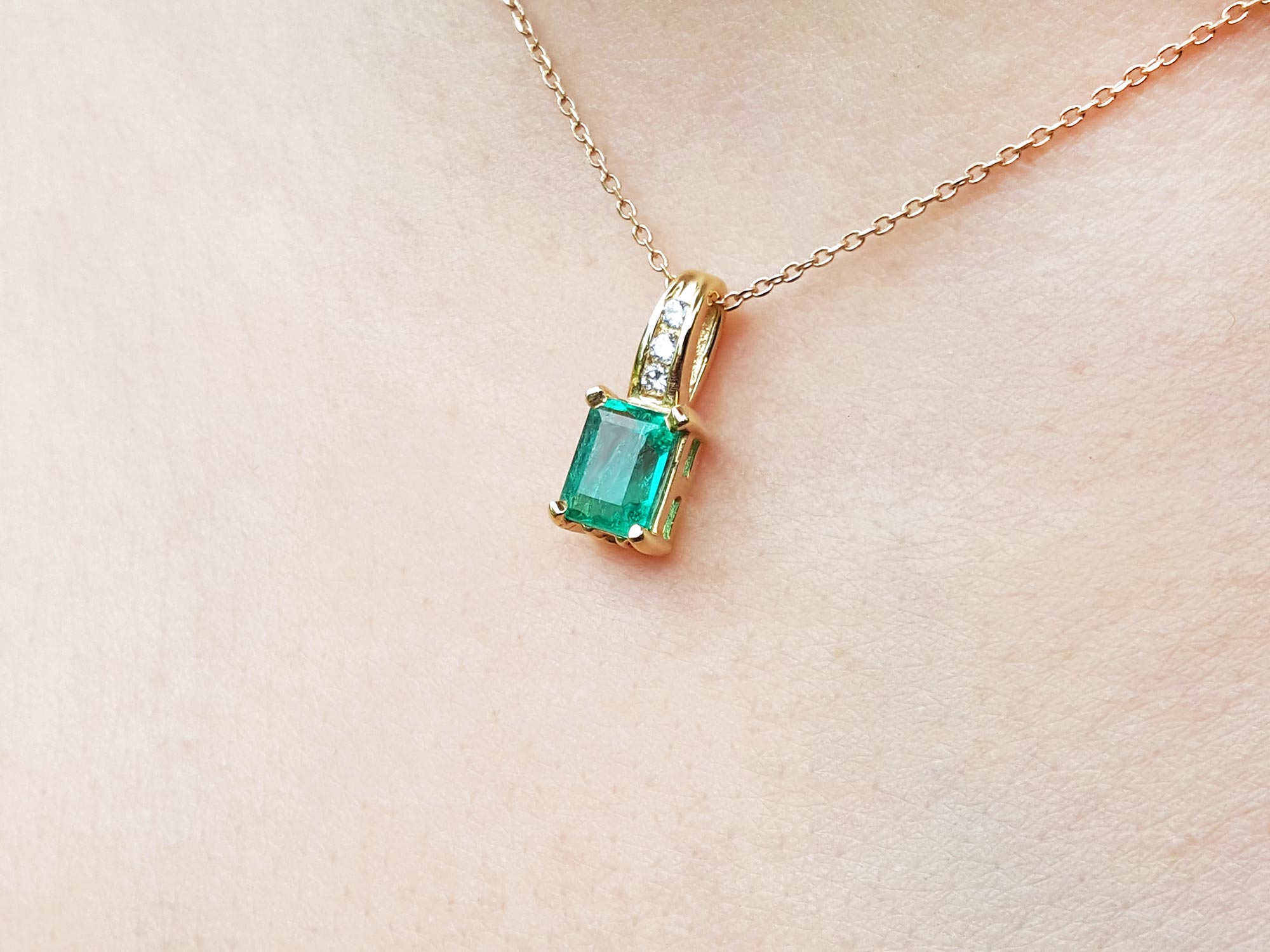 A left side position of an emerald and diamond pendant with yellow gold necklace on a skin background