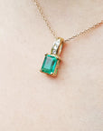 A left side position of an emerald and diamond pendant with yellow gold necklace on a skin background