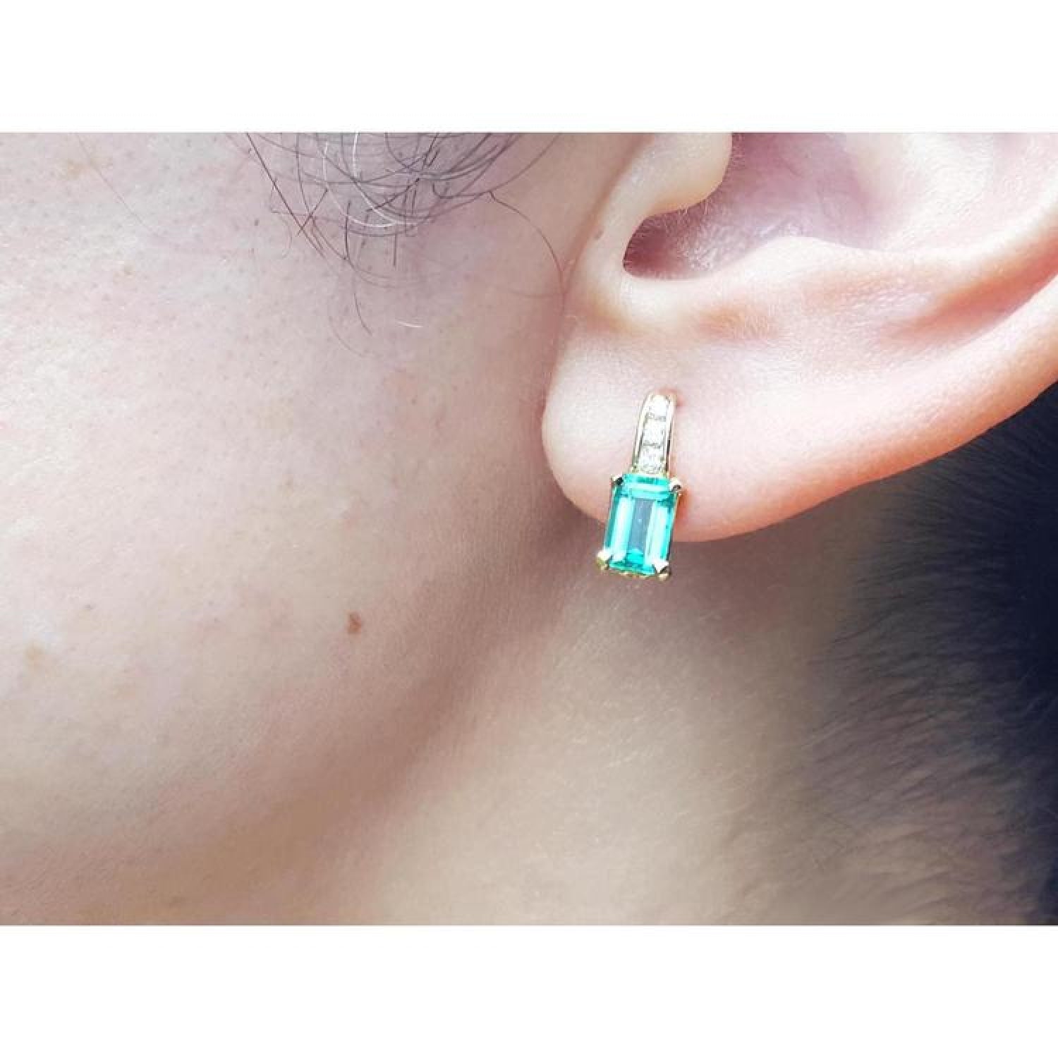 Emerald cut emerald earring in 14K yellow gold on an earlobe.