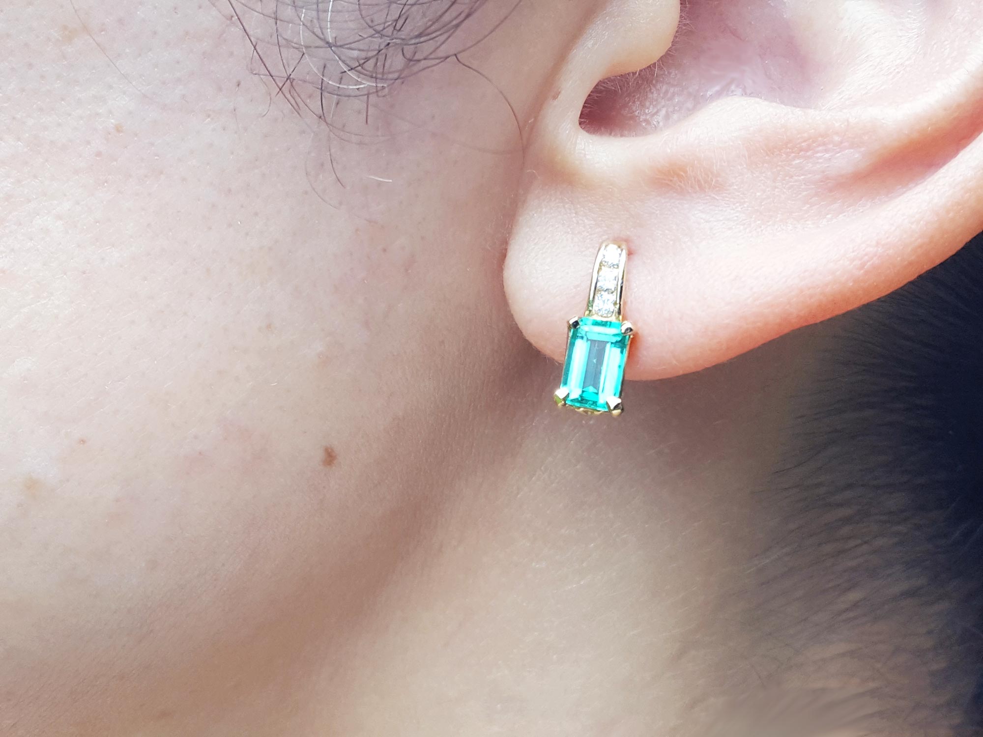 A woman&#39;s ear Wearings a natural emerald earring in yellow gold