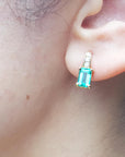 A woman's ear Wearings a natural emerald earring in yellow gold