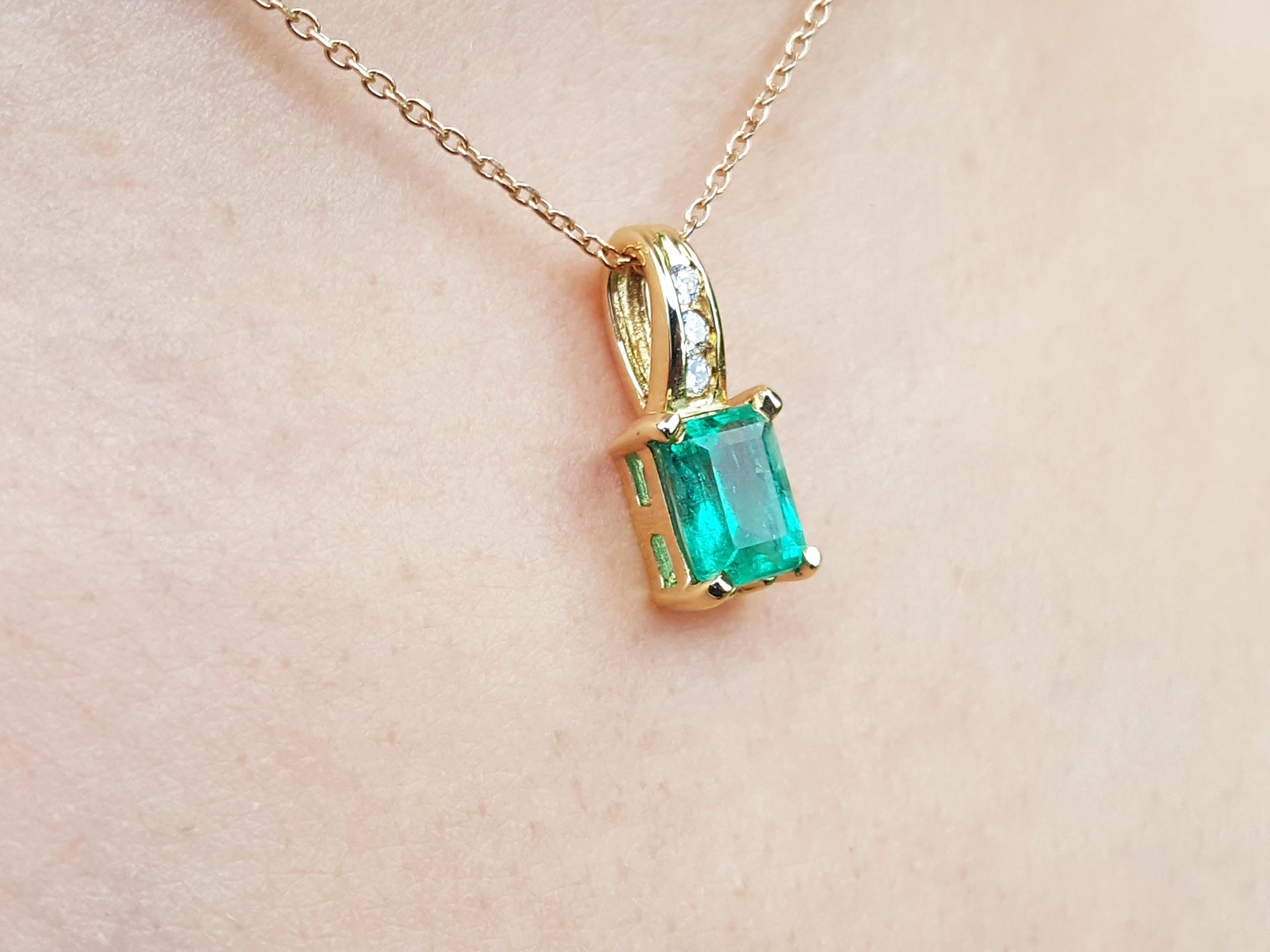A right-side profile view of an emerald pendant on a skin background