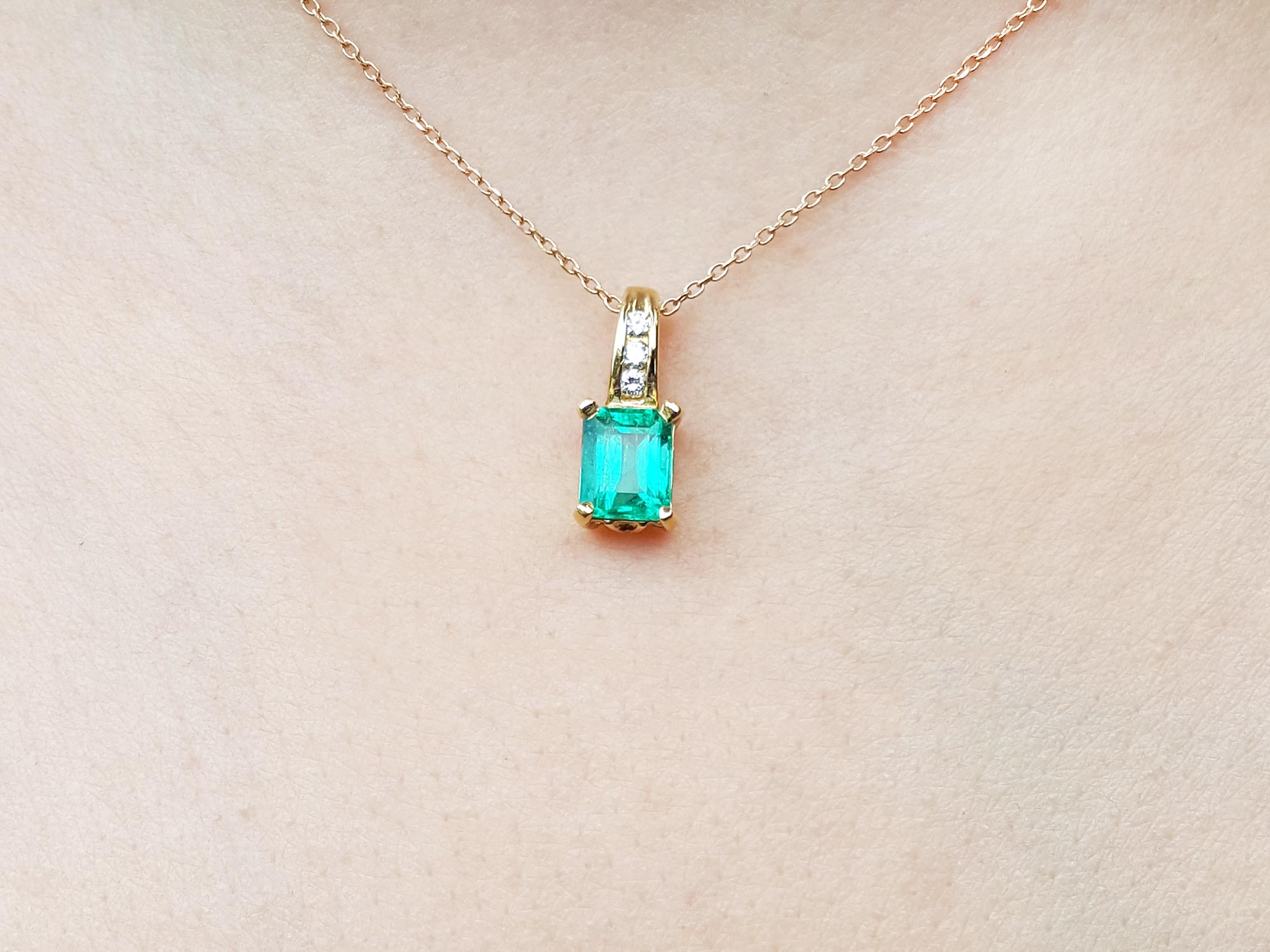 A 14k yellow gold necklace with an emerald pendant on a skin background