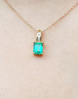 A 14k yellow gold necklace with an emerald pendant on a skin background