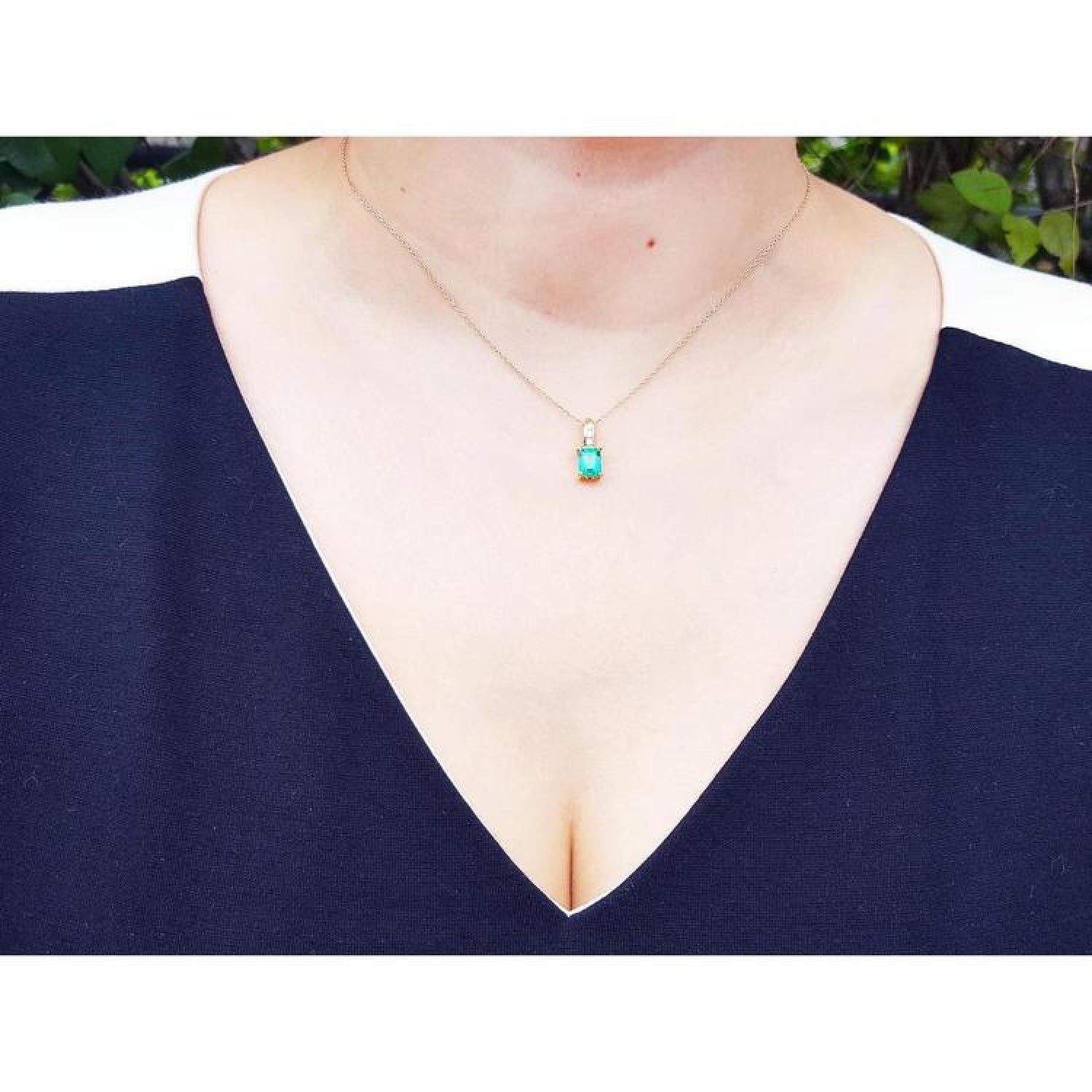 Emerald pendant on a delicate 14K yellow gold chain, worn by a person in a black and white top.