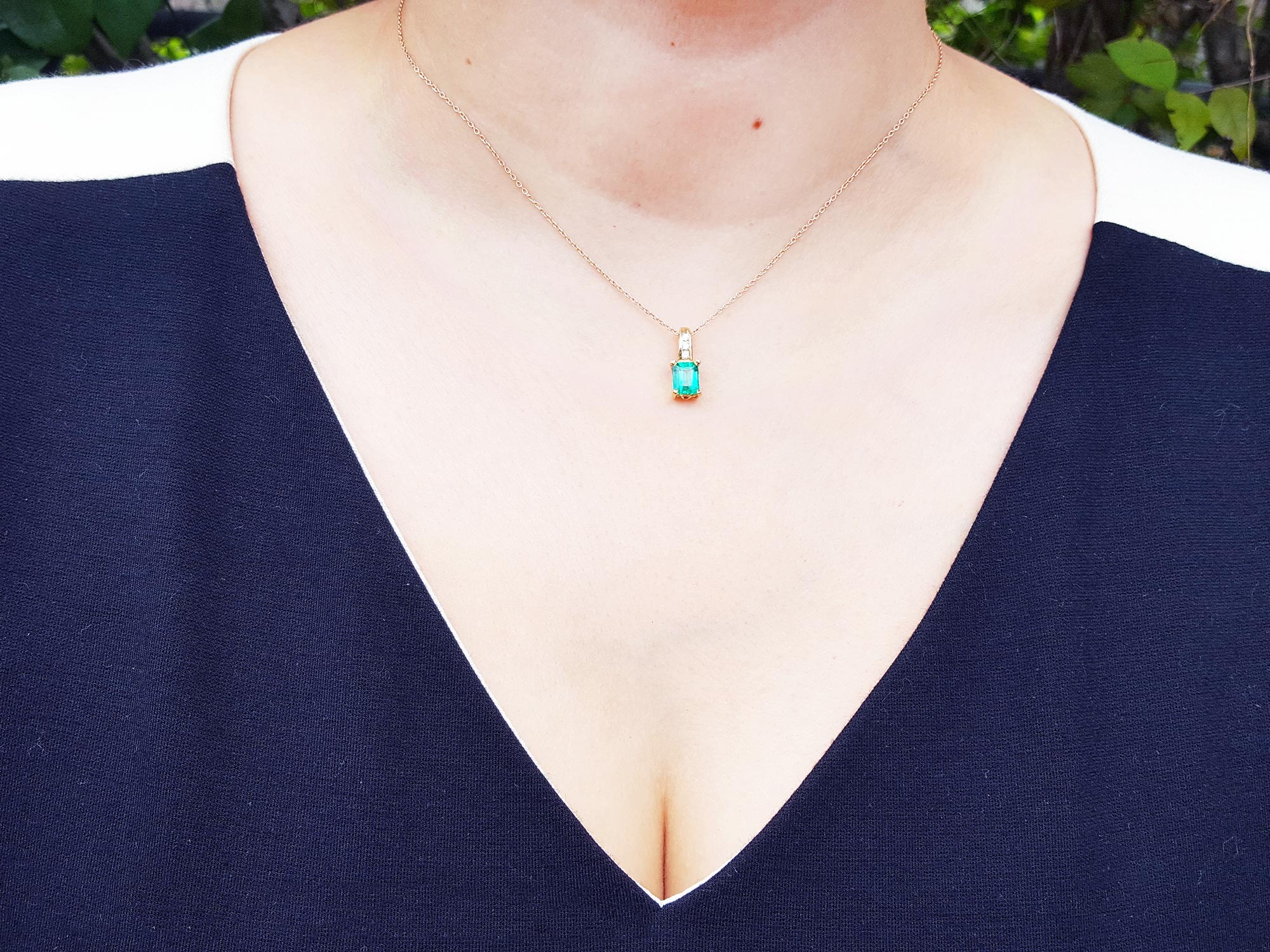 A woman wearing a yellow gold necklace with a natural emerald pendant, dressing a blue top