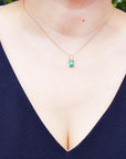 A woman wearing a yellow gold necklace with a natural emerald pendant, dressing a blue top