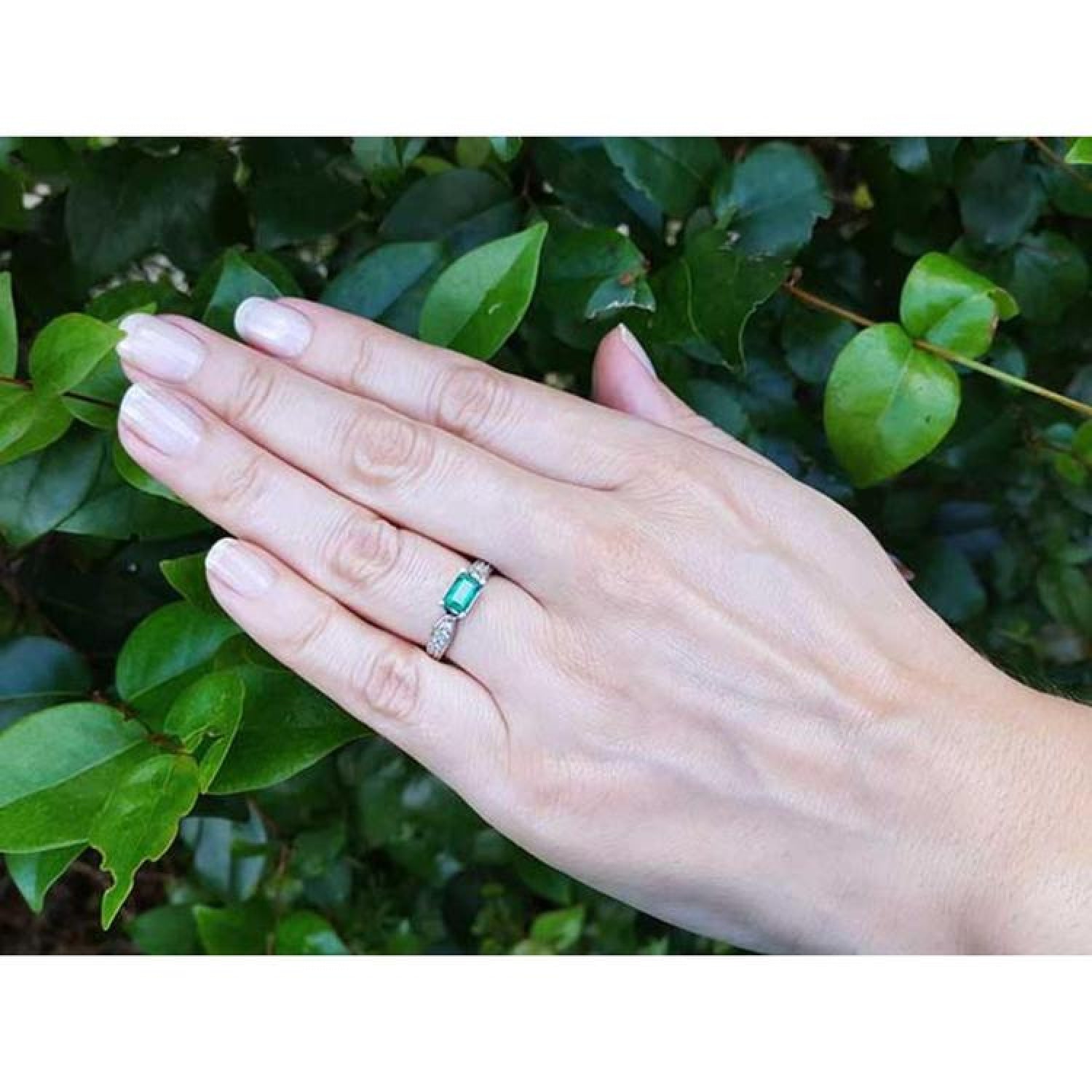 East-west emerald cut Colombian emerald ring in 14k white gold with diamond accents on a hand.