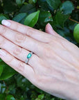 Hand wearing a Mother's Day gift emerald ring against a green leafy background.