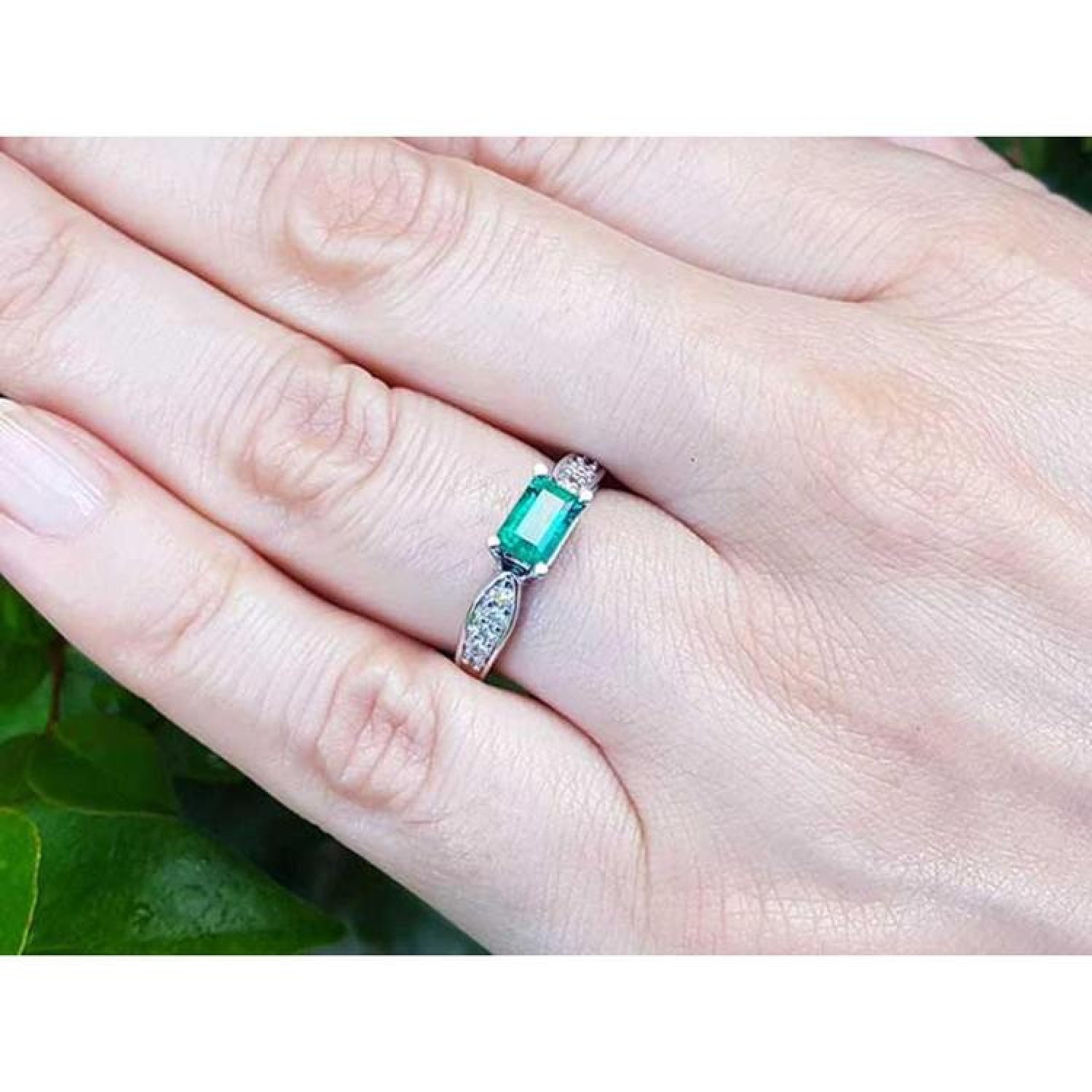0.90 ct. East West emerald ring in 14k white gold with diamond accents, worn on a hand.