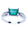 A colombian emerald ring east-west style with accent diamonds in white gold, top and sides profile view.