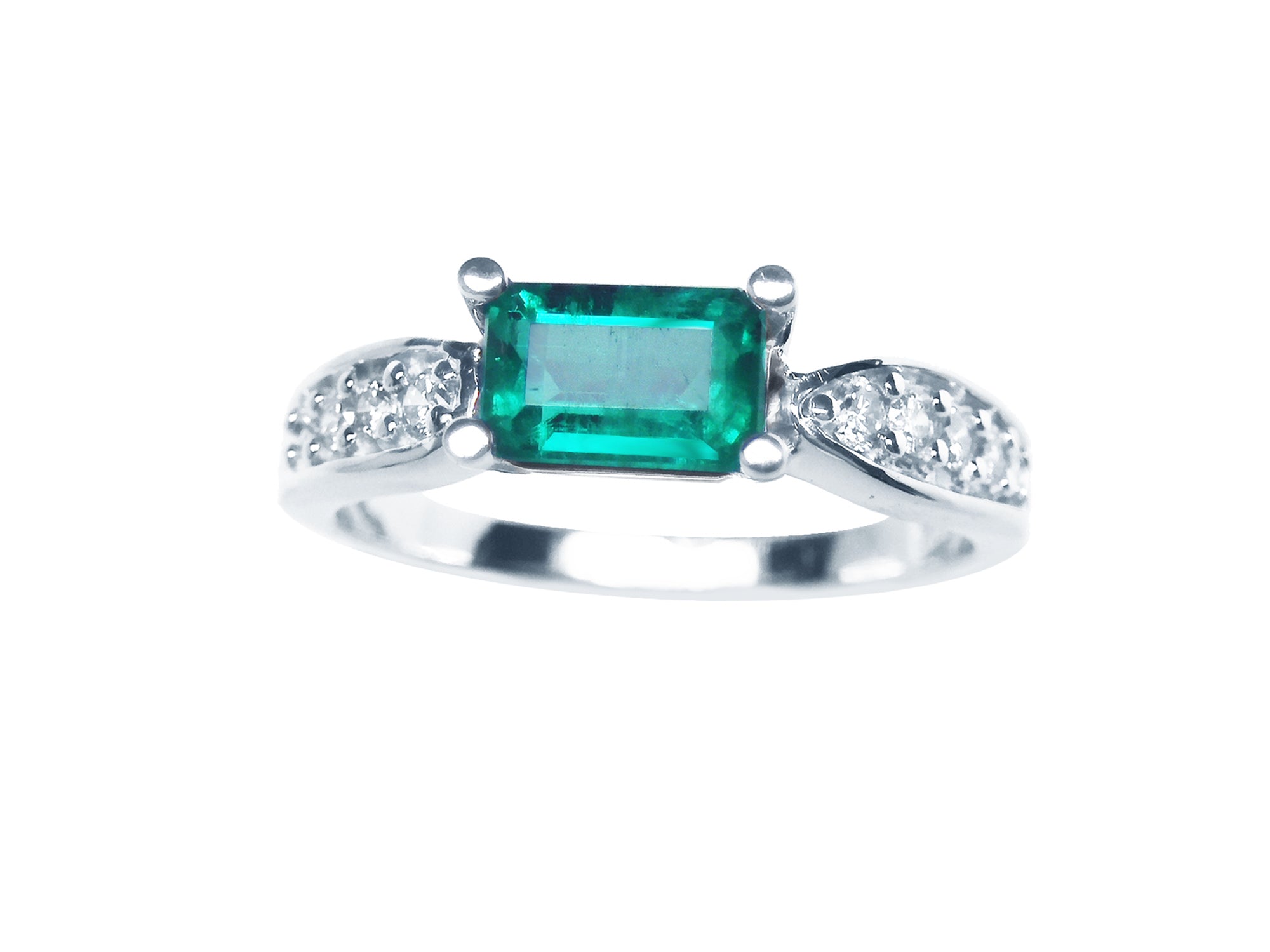A white gold emerald ring wast-west style with accent diamonds on the band, top profile view.