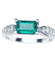 A white gold emerald ring wast-west style with accent diamonds on the band, top profile view.