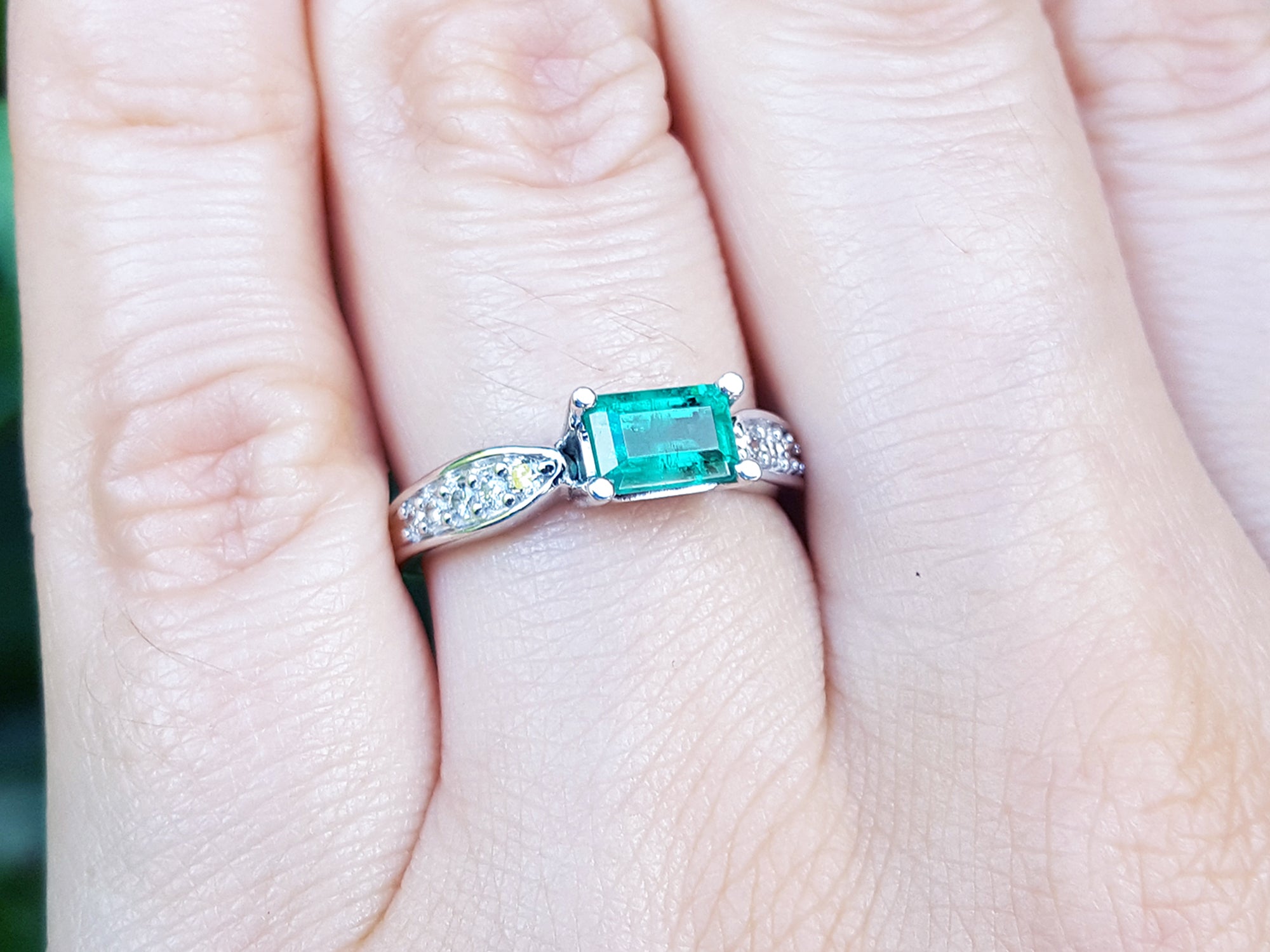 Emerald ring with diamonds on a hand against a blurred green background