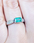 Emerald ring with diamonds on a hand against a blurred green background