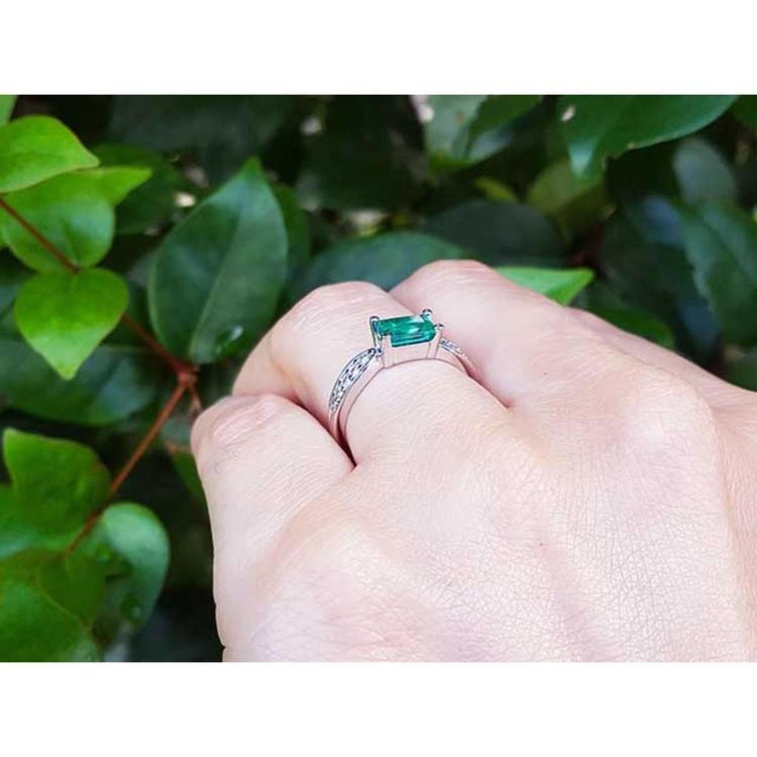 East-west emerald ring with a vivid green stone and diamond accents on a 14k white gold band.