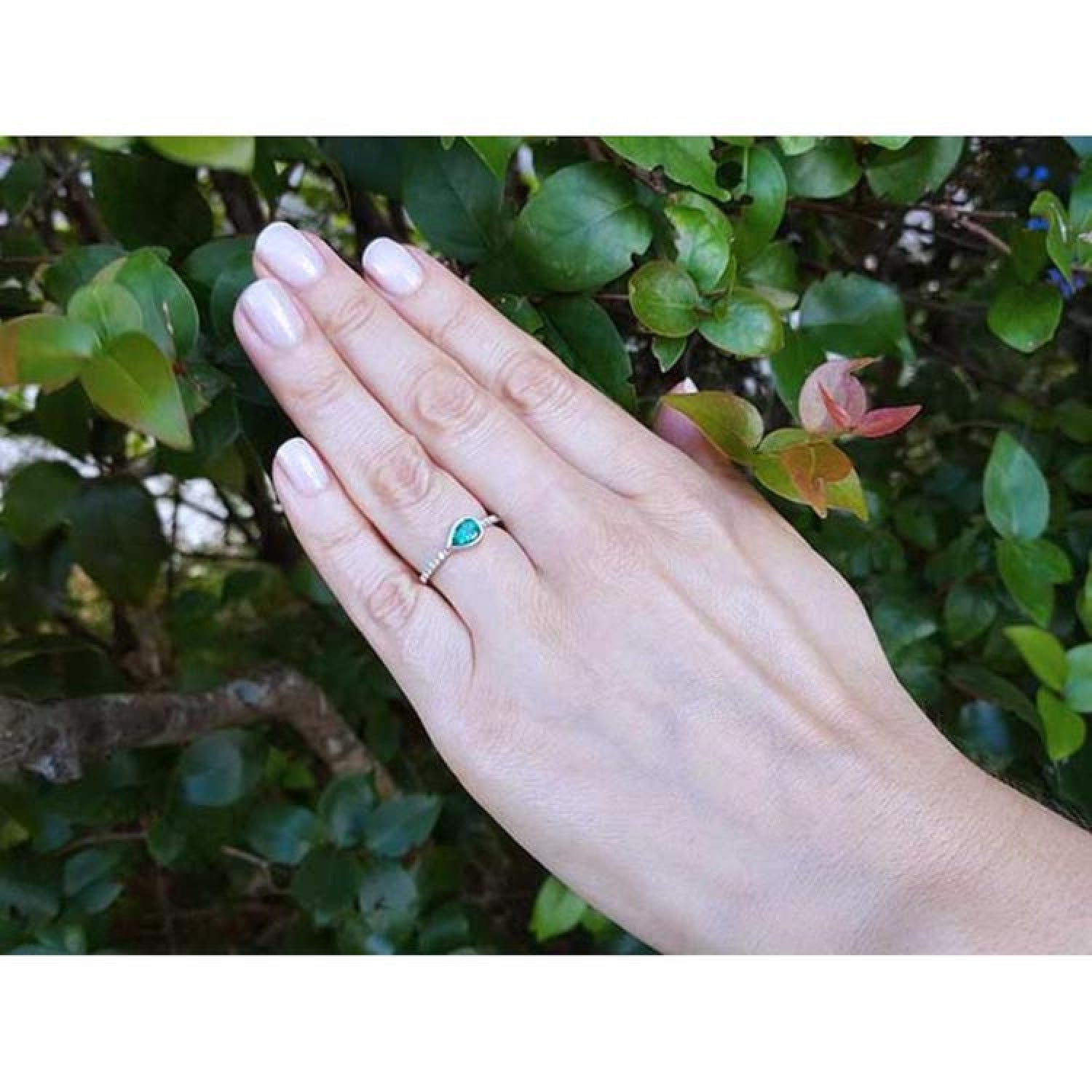 14K white gold ring with a bezel-set east-west teardrop emerald and diamond accents.