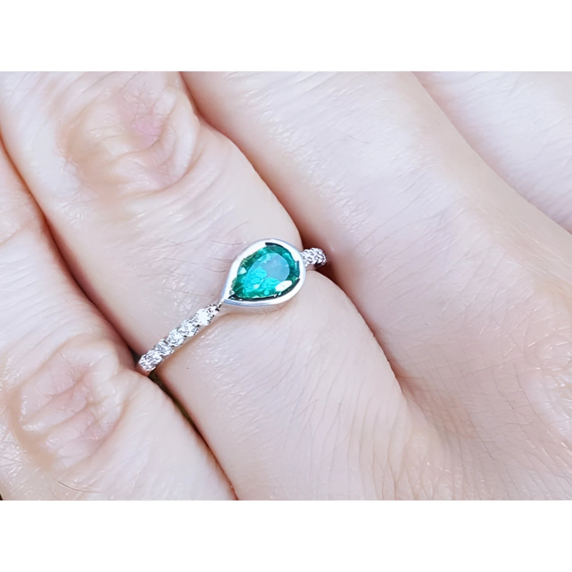 East-west teardrop emerald ring with bezel setting and diamond-accented 14K white gold band.