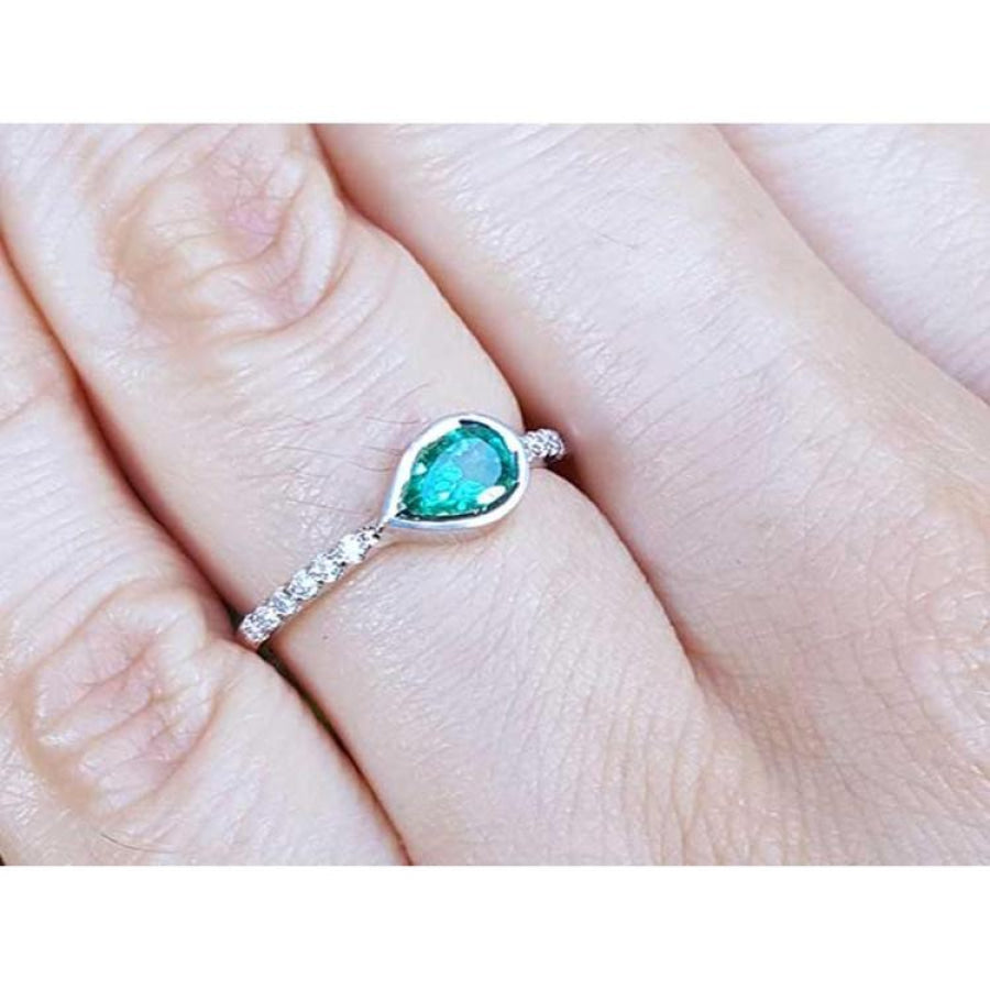 East-west teardrop emerald ring with bezel setting and diamond-accented 14K white gold band.