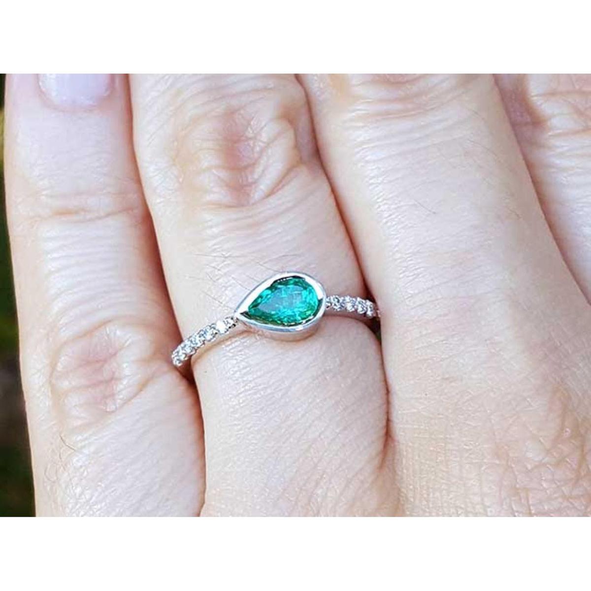 A pear cut natural colombian emerald ring with diamonds accent on a finger.