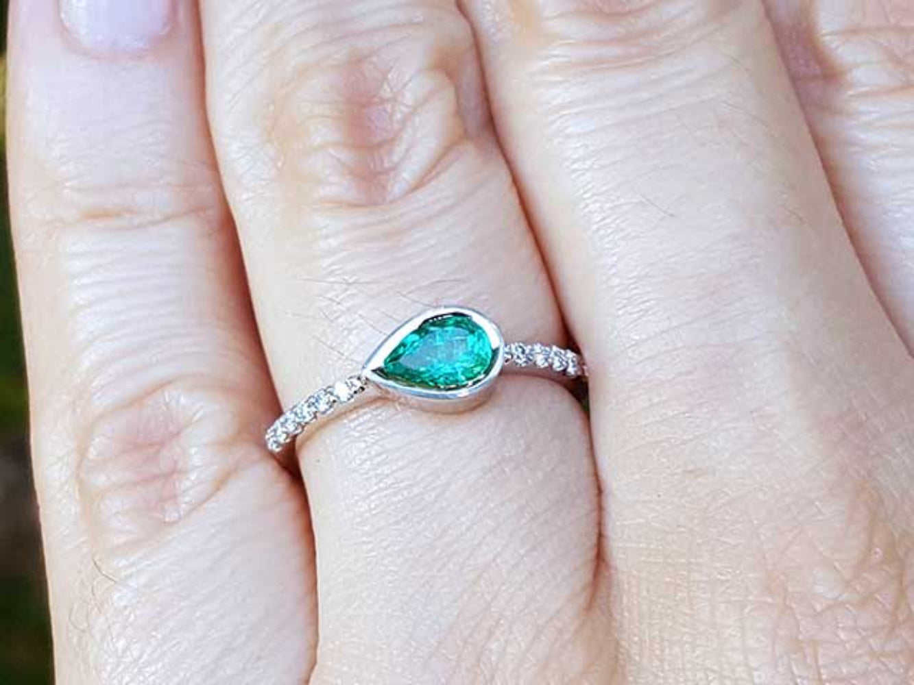 A pear cut natural colombian emerald ring with diamonds accent on a finger.