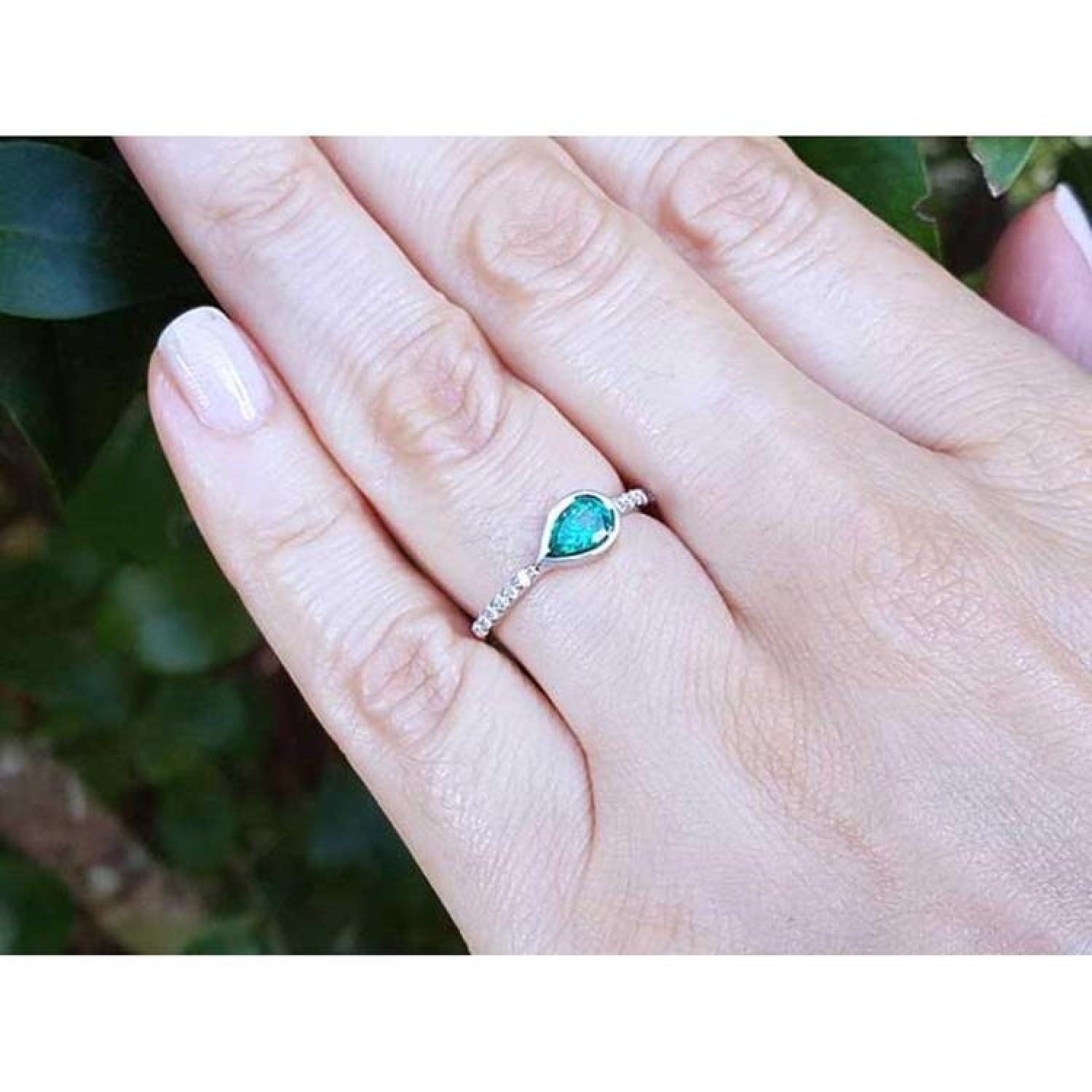 14K white gold ring with a bezel-set east-west teardrop emerald and diamond accents.