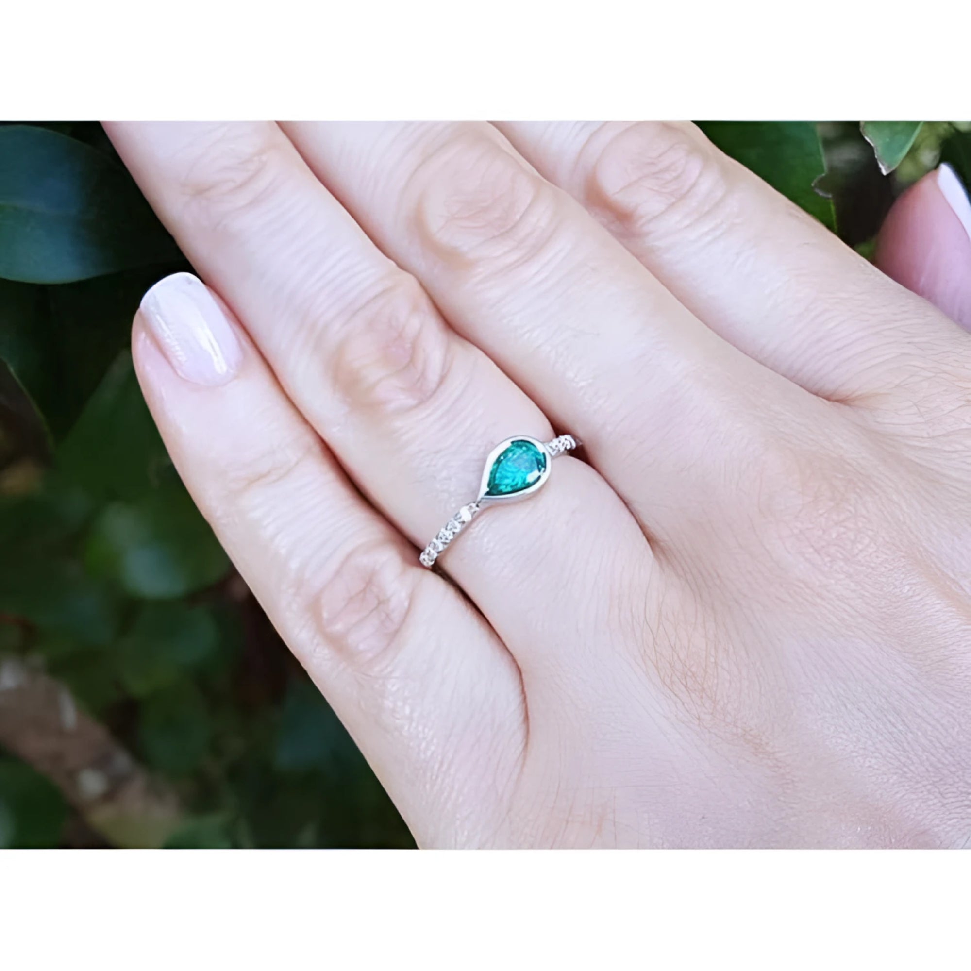 14K white gold ring with a bezel-set east-west teardrop emerald and diamond accents.