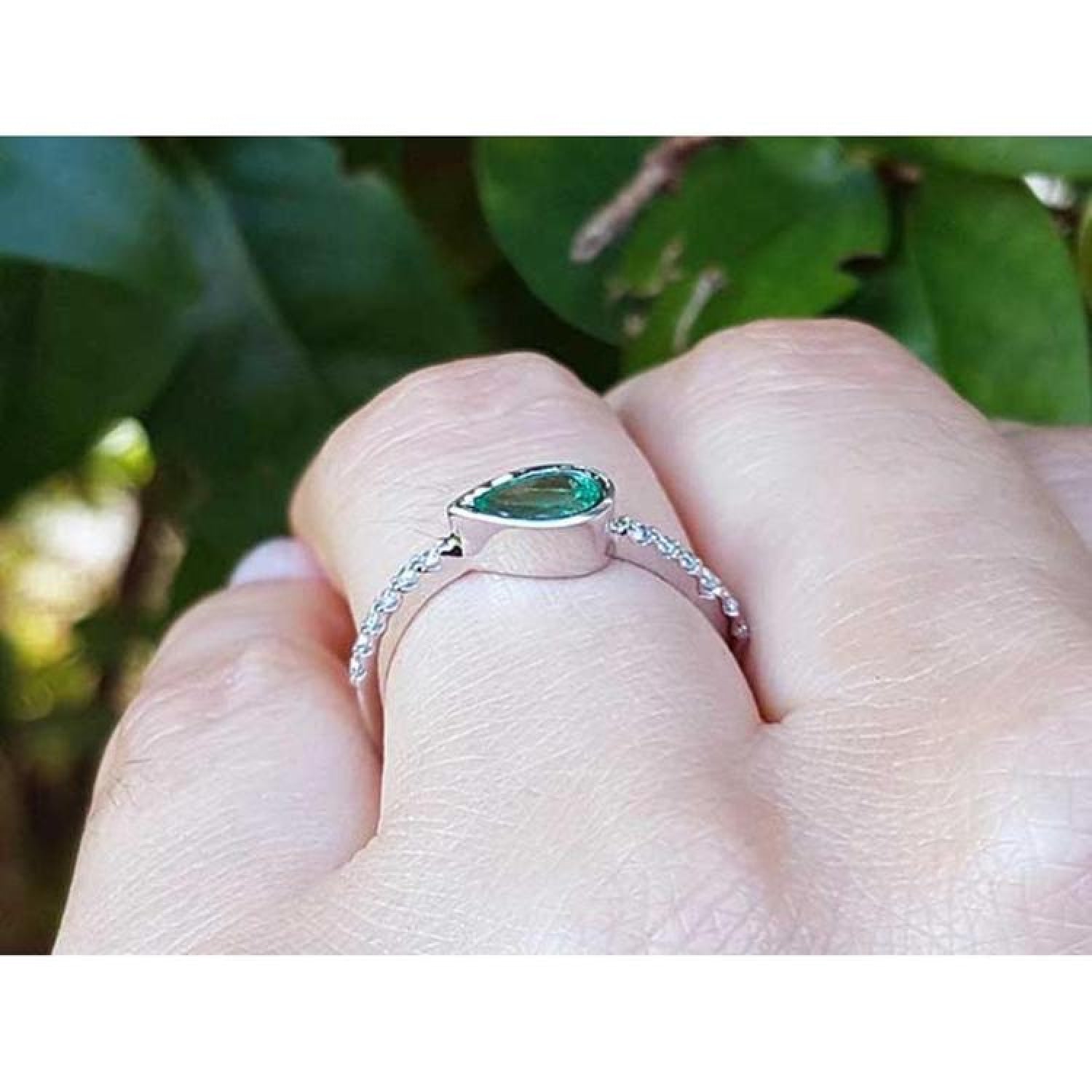 14K white gold ring with a bezel-set east-west teardrop emerald and diamond accent band.