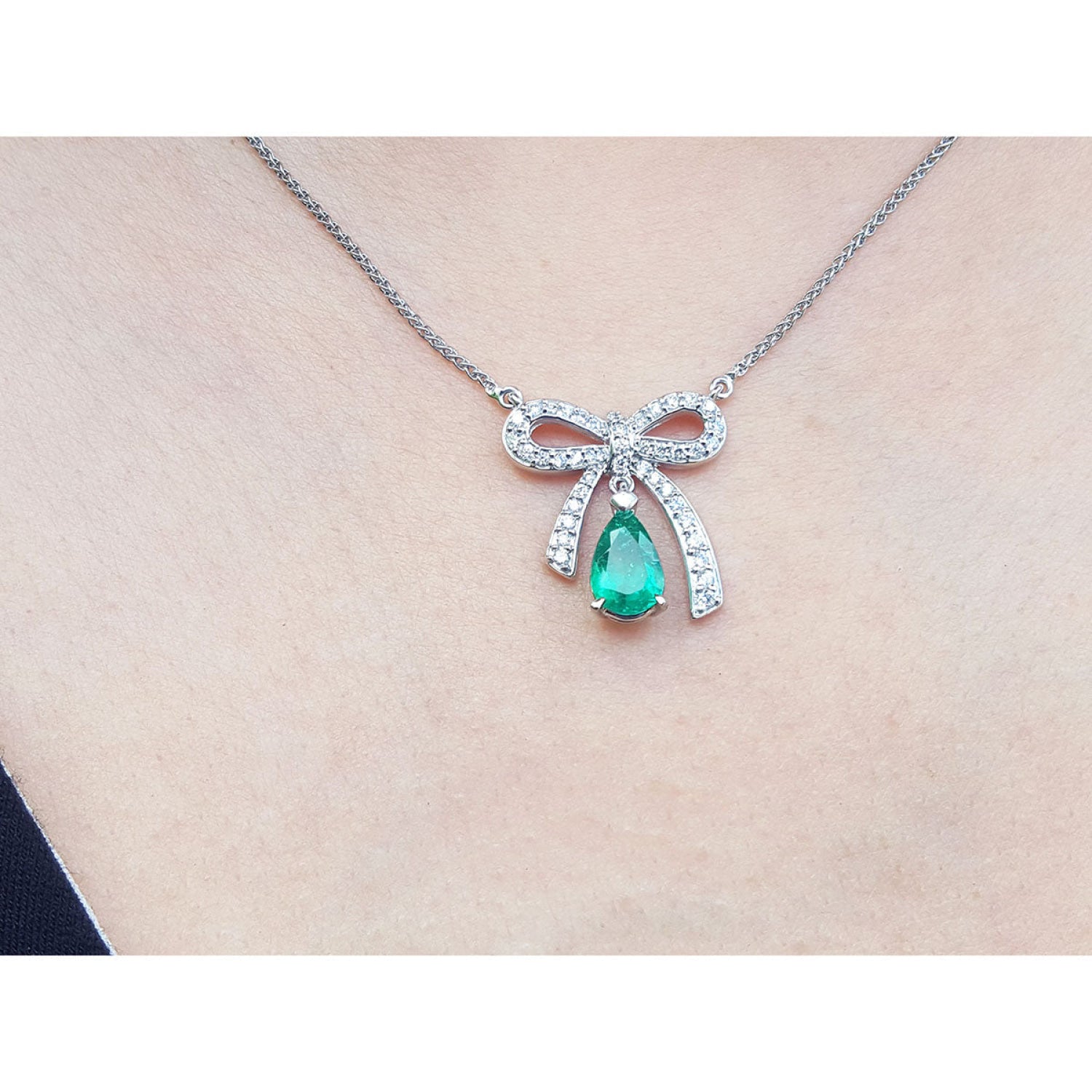 18K white gold bow-tie necklace with pear-shaped emerald and diamonds on a chain.