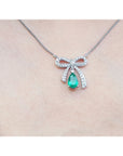 18K white gold bow-tie necklace with pear-shaped emerald and diamonds on a chain.