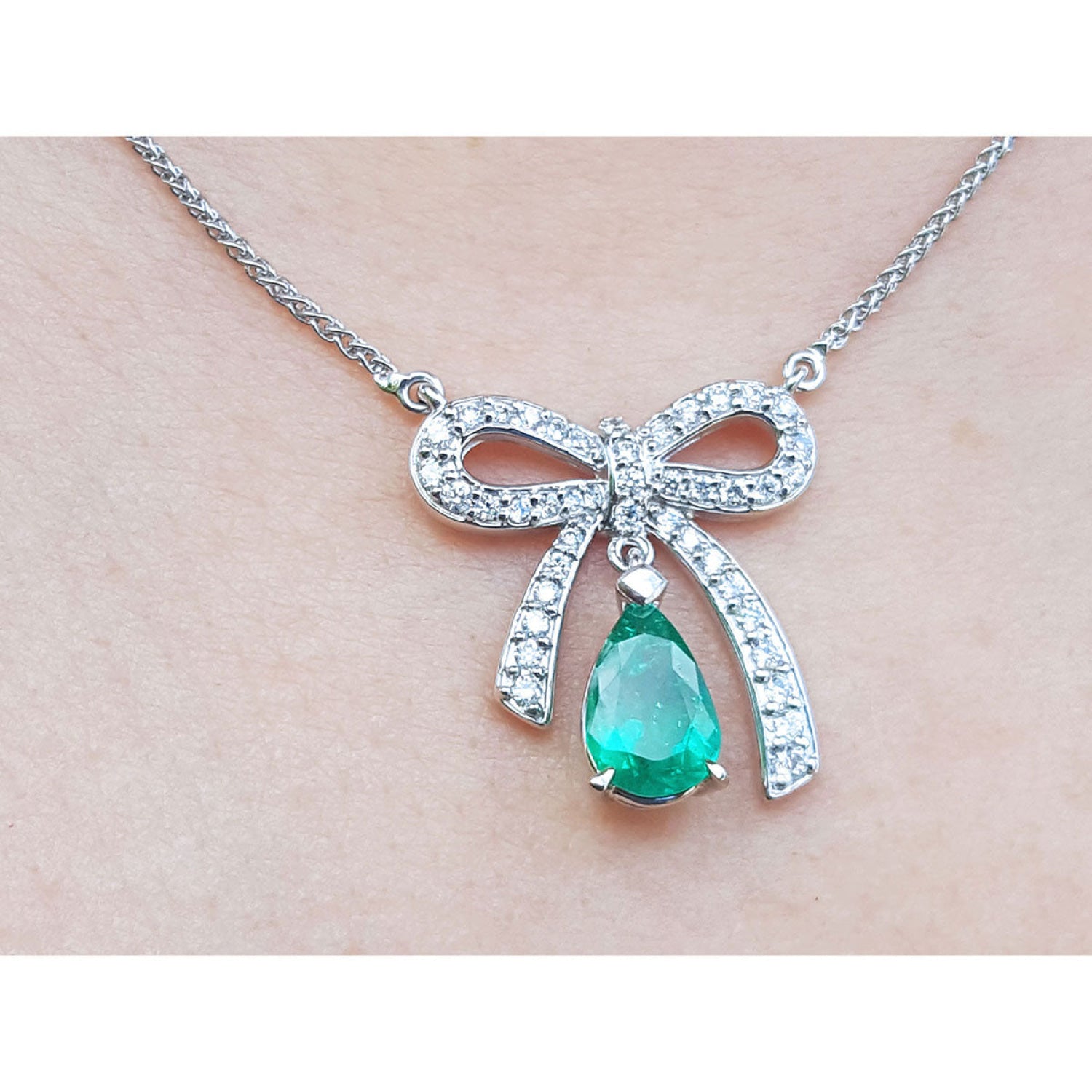 18K white gold bow-tie necklace with a pear-shaped deep green emerald pendant.