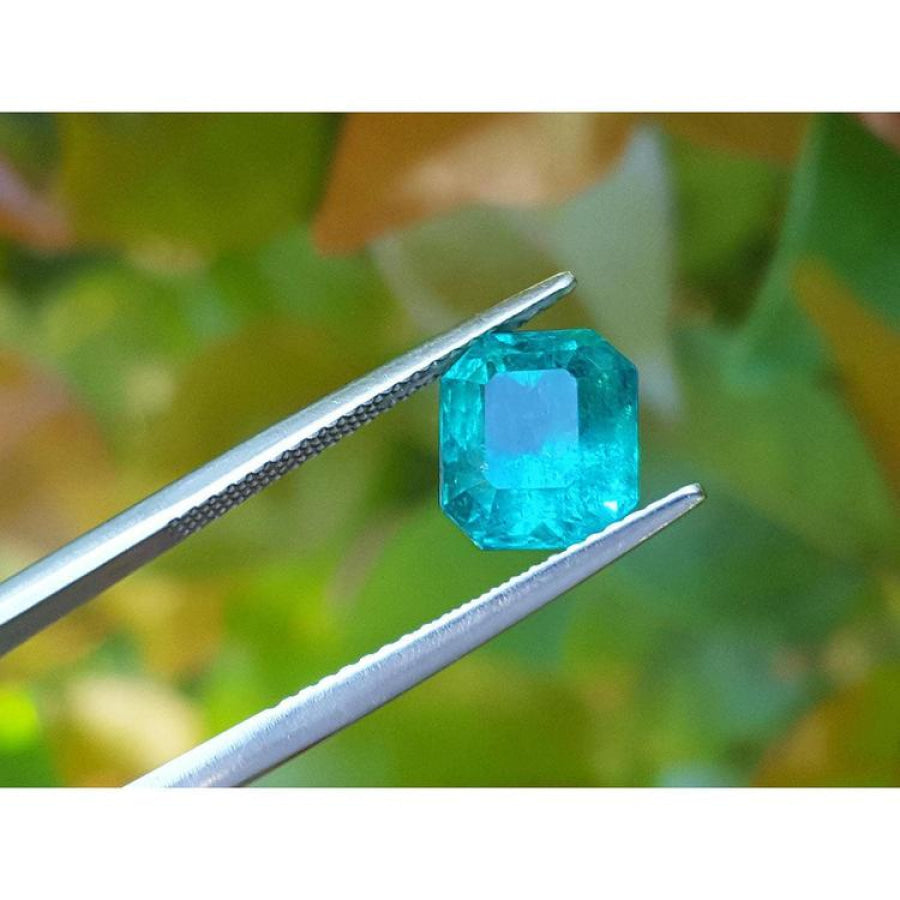 2.95 ct square natural Colombian emerald with bright medium green hue held by tweezers.