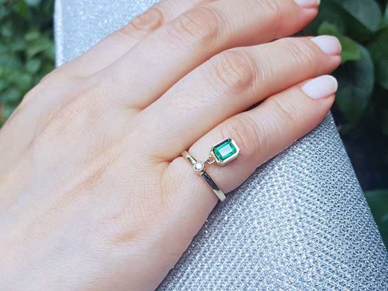 Hand wearing a gold emerald dangle ring on a purse.