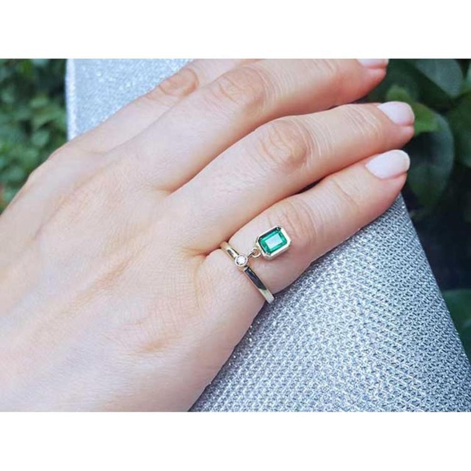 14K yellow gold ring with a bezel-set emerald dangle and small diamond accent on a finger.