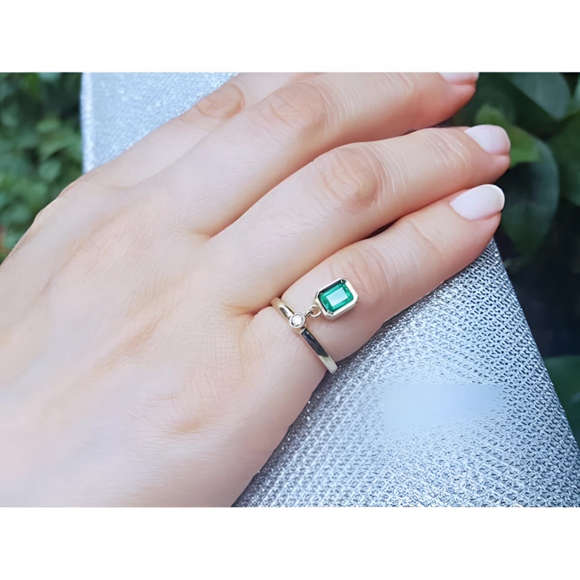 14K yellow gold ring with a bezel-set emerald dangle and small diamond accent on a finger.