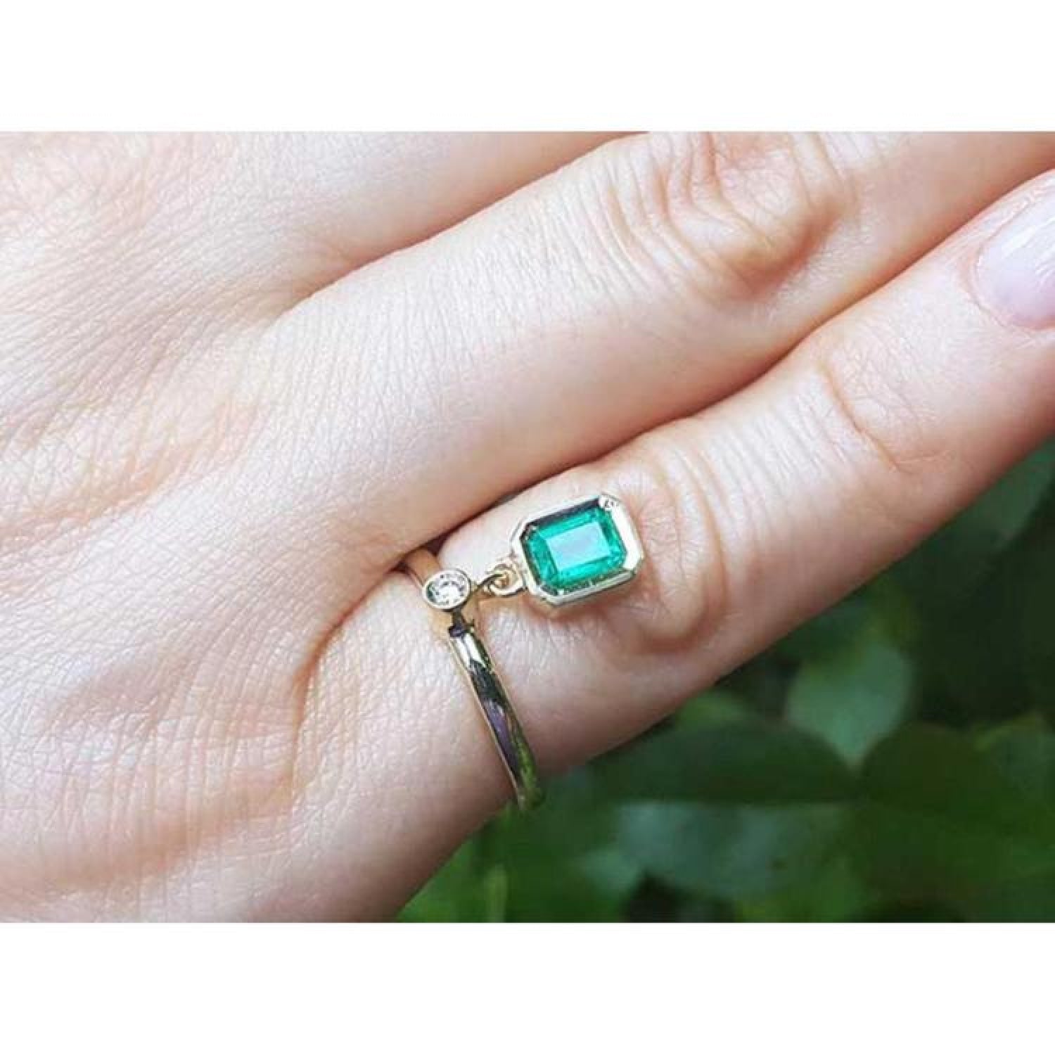 14K yellow gold ring with a bezel-set emerald dangle and small diamond accent on a finger.