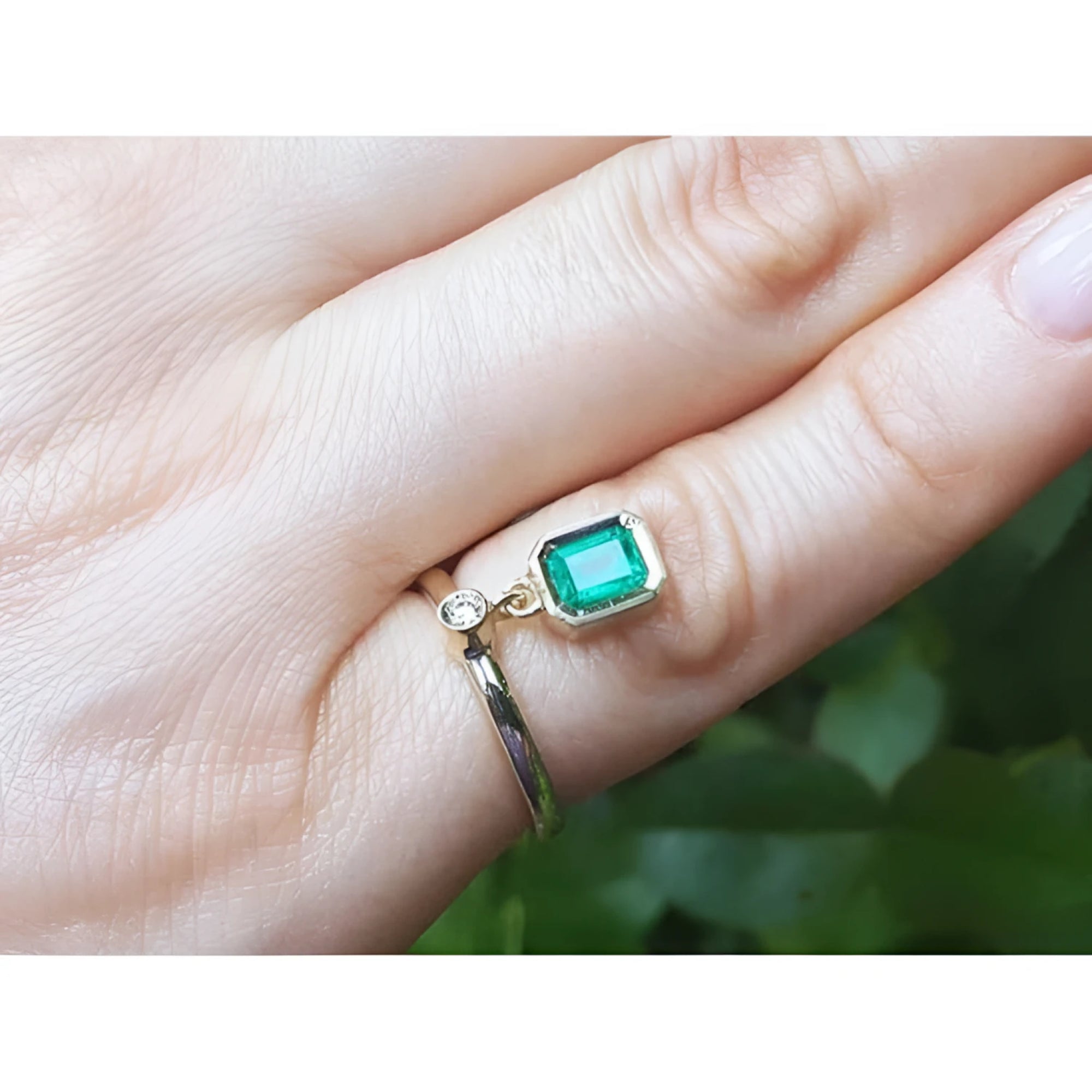 14K yellow gold ring with a bezel-set emerald dangle and small diamond accent on a finger.