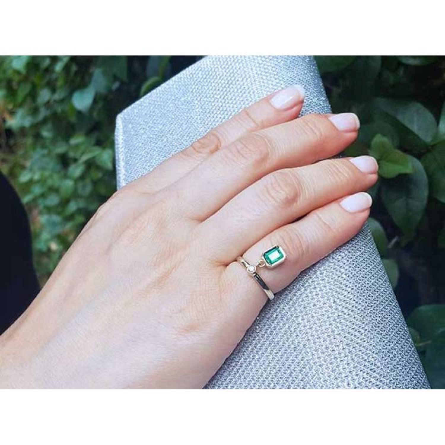 14K yellow gold ring with a bezel-set emerald dangle and small diamond accent on a hand.