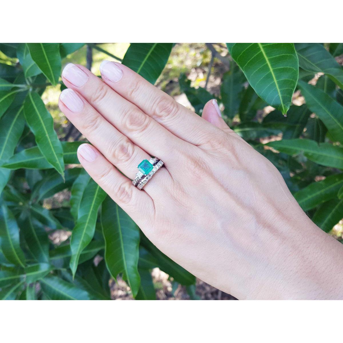 Hand wearing an emerald ring with a match band against a green leafy background.