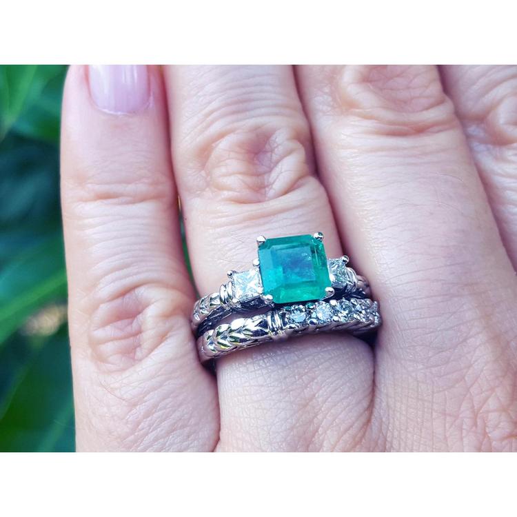 A hand wearing an emerald ring with matching wedding band made of 14k white gold.