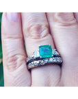 A hand wearing an emerald ring with matching wedding band made of 14k white gold.
