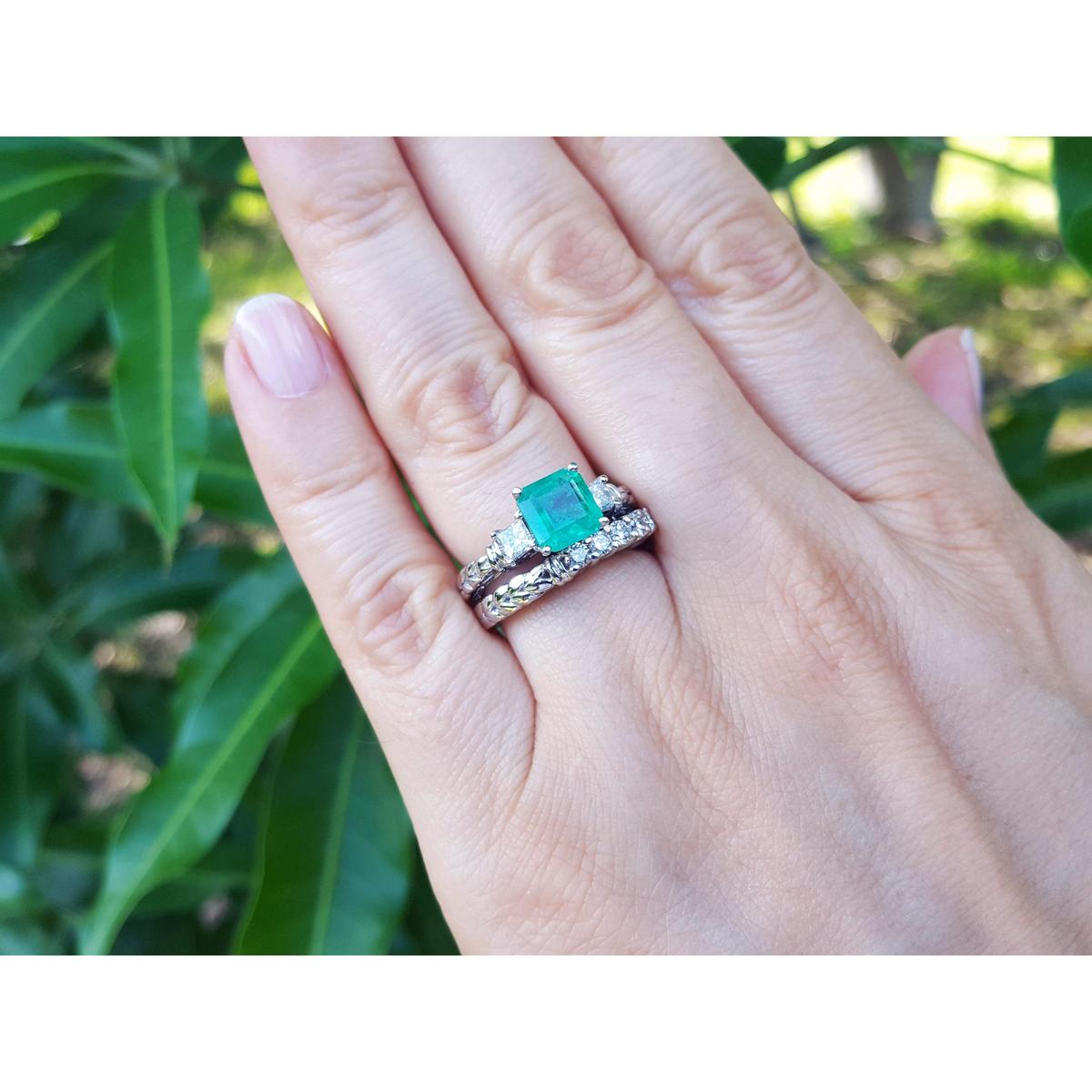 A close-up of a emerald and wedding band ring set on a green leafy background.