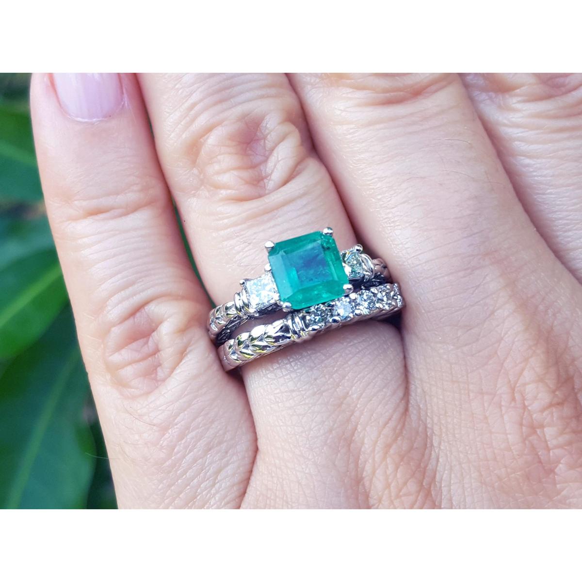 A finger wearing a macht set of emerald ring and diamond wedding band in white gold.