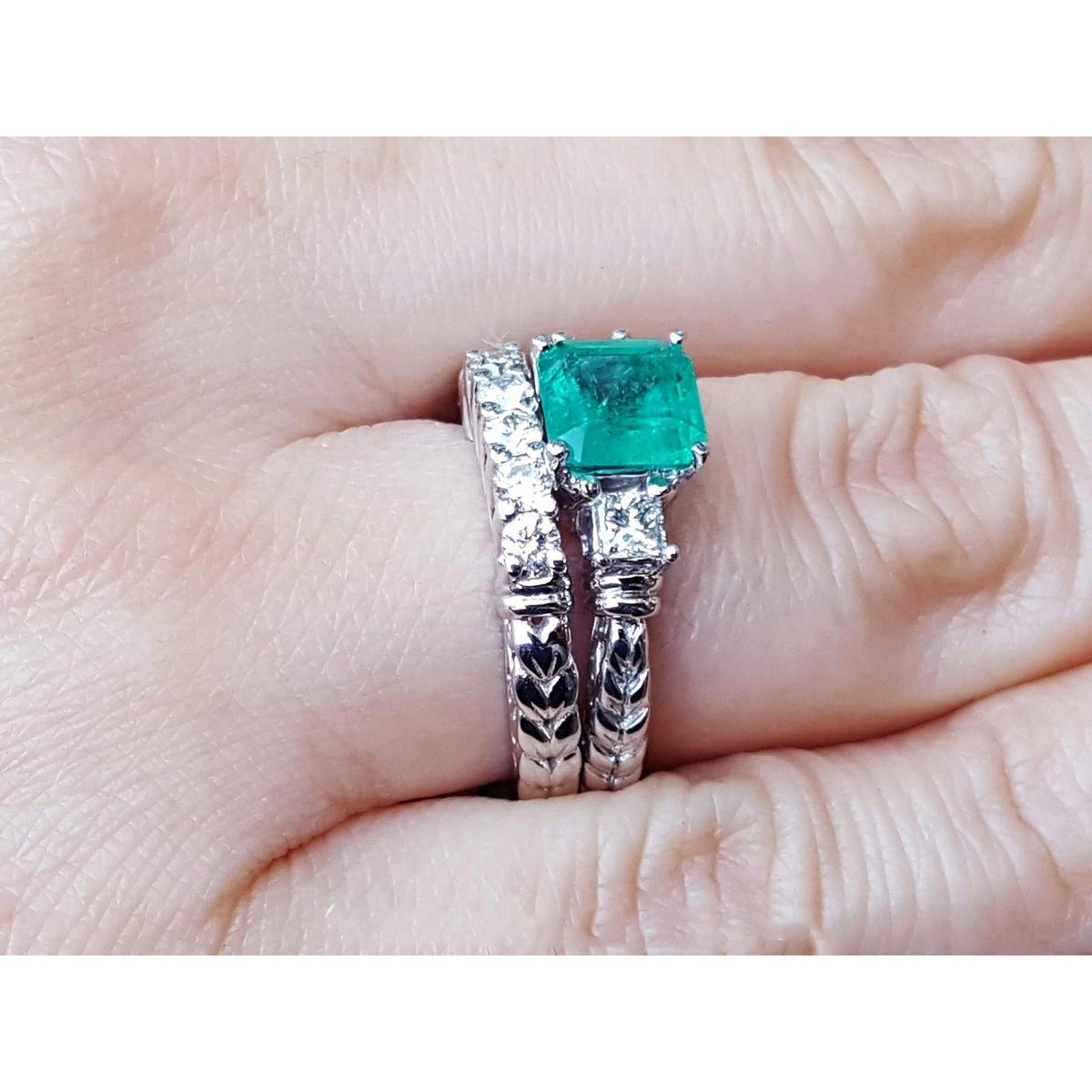 Side view of a finger wearing a matcht set emerald ring and wedding band in white gold.