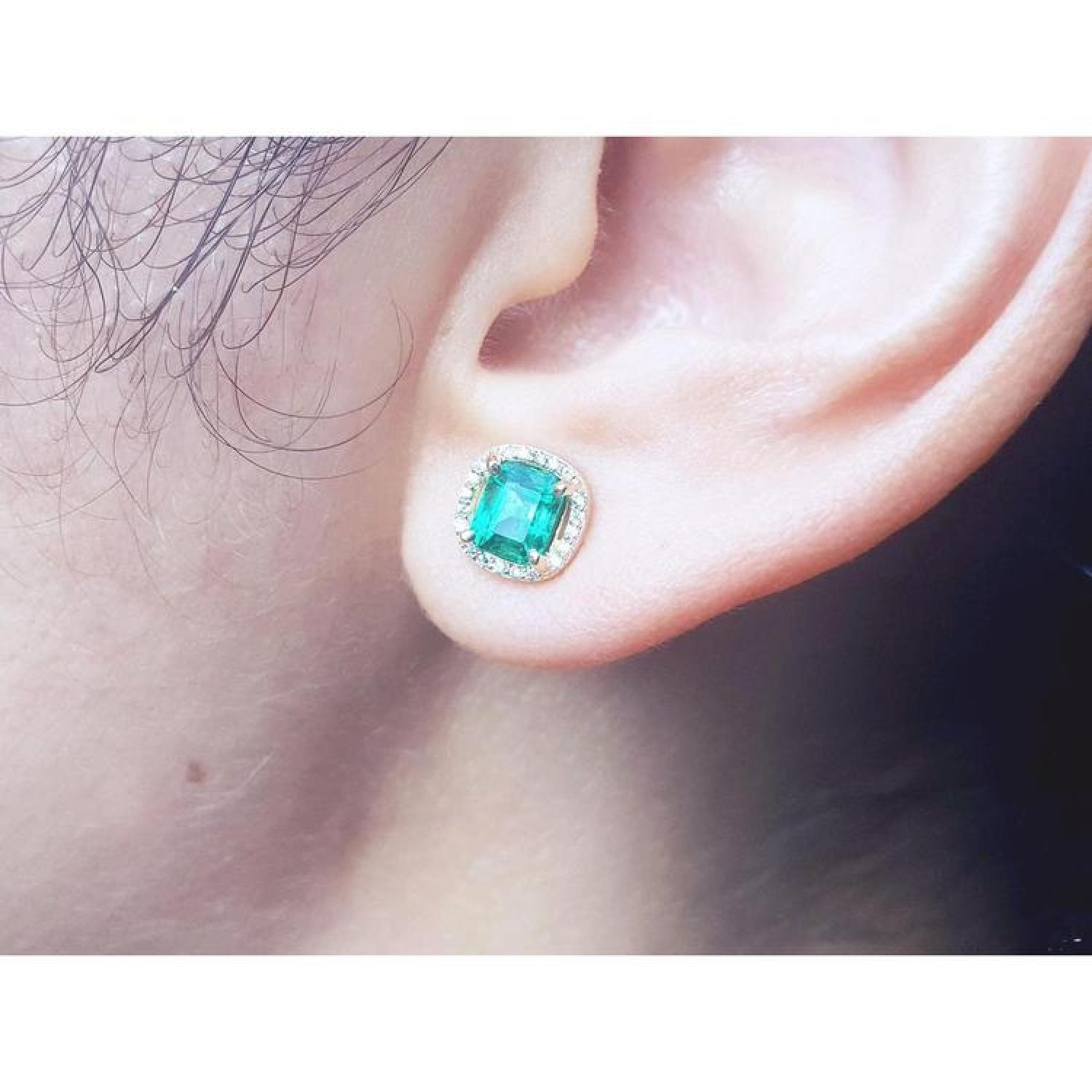 1.55 carat emerald halo diamond stud earring in 14K yellow gold on an ear.