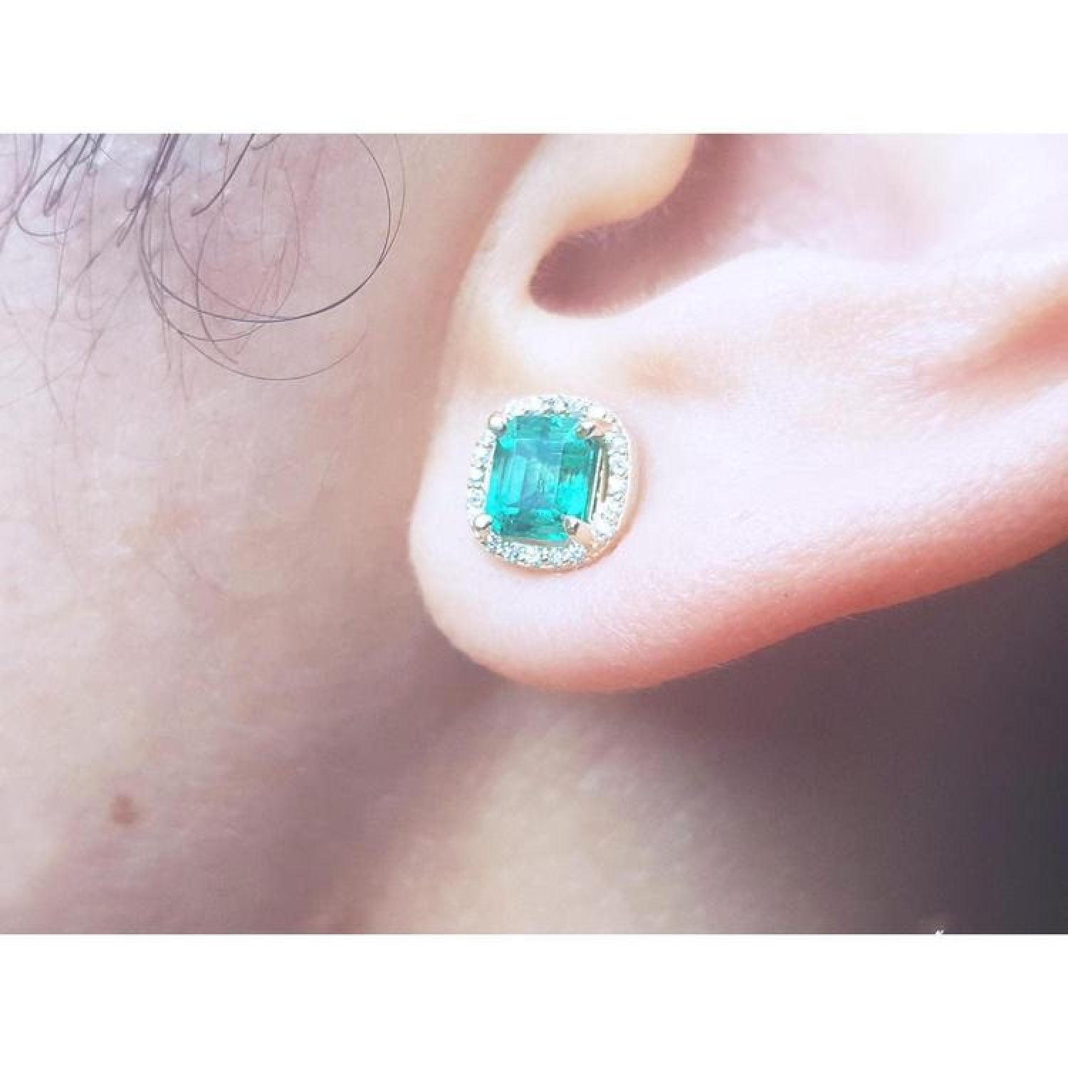 1.55 carat emerald stud earring with halo diamonds, set in 14K yellow gold, worn on an ear.