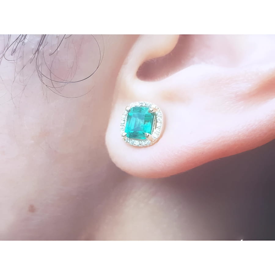 1.55 carat emerald stud earring with halo diamonds, set in 14K yellow gold, worn on an ear.